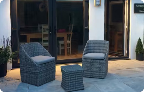Outdoor patio with wicker chairs and table near glass doors, evening setting.