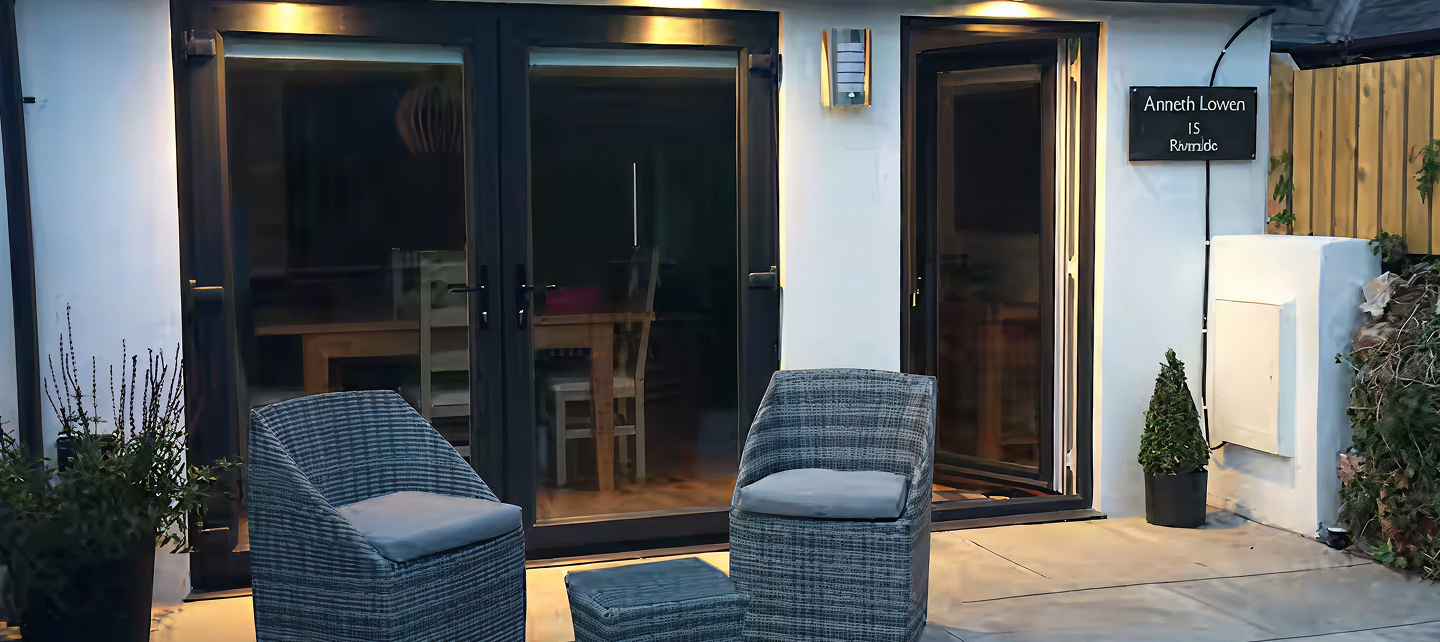 Cozy outdoor seating area with wicker chairs, modern glass doors, and soft lighting in a welcoming setting.