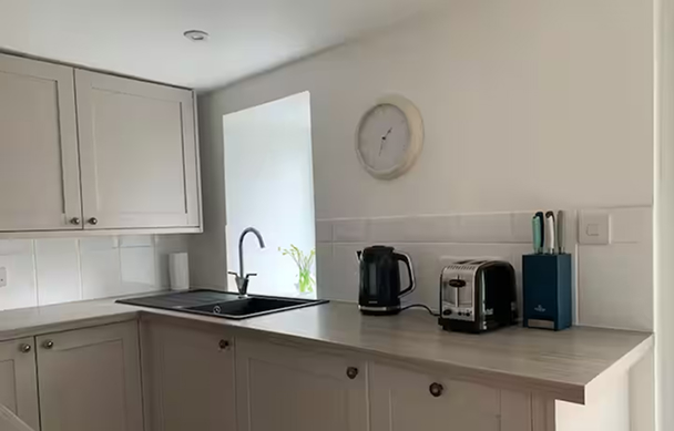 Modern kitchen countertop with sink, toaster, kettle, and knife set under a wall clock. Minimalist design.