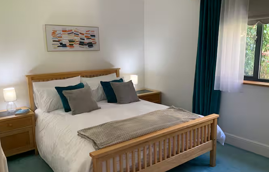 Cozy bedroom with wooden frame bed, teal cushions, and abstract wall art, featuring natural light from a window with