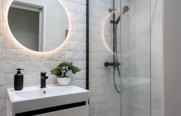 Modern bathroom with round mirror, stylish white sink, potted plant, and glass shower enclosure.