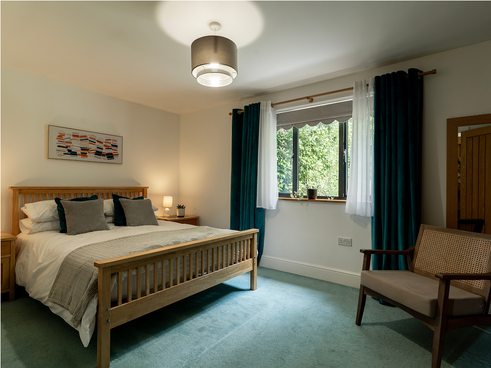 Cozy bedroom with natural light, wooden furniture, teal curtains, and stylish decor. Comfortable and inviting design.