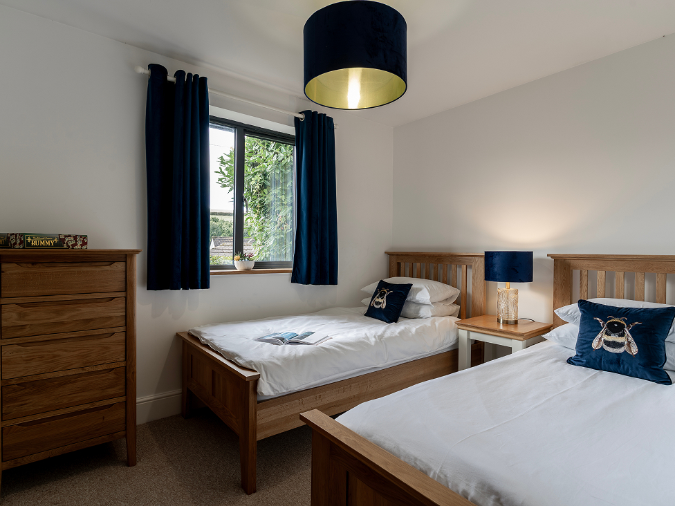Cozy twin bedroom with wooden furniture, bee-themed decor, and a window view. Navy curtains and bedding accents.