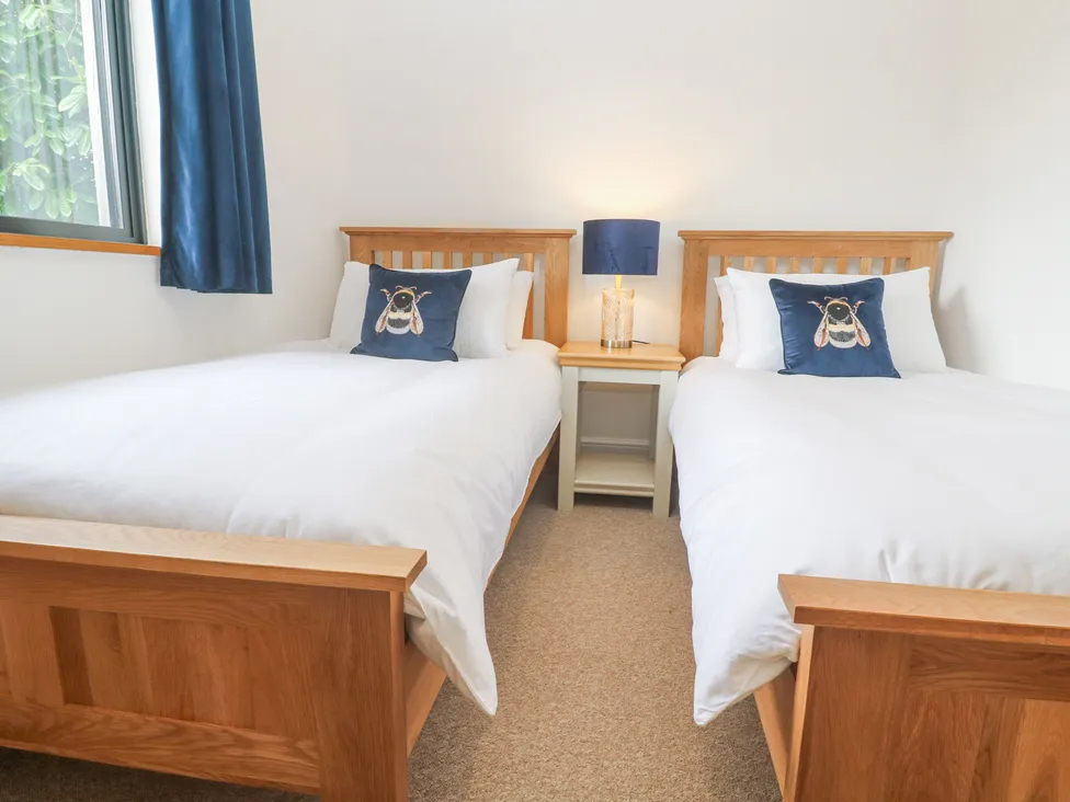 Twin beds with wooden frames, adorned with bee-themed pillows, blue lamp, and window curtains in a cozy bedroom.