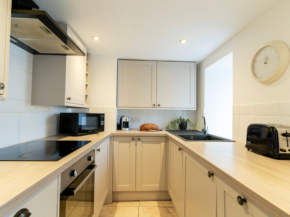 Modern kitchen interior with beige cabinets, black appliances, and countertop bread, plant, and clock. Bright and organized.