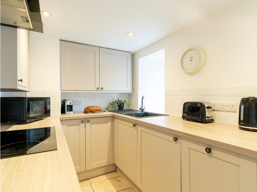 Modern kitchen with light wood cabinets, a countertop clock, black appliances, and a loaf of bread next to a plant.