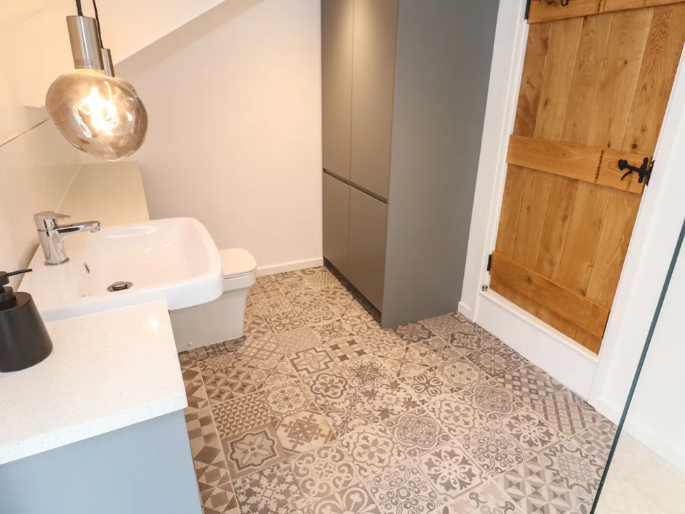 Modern bathroom with patterned tiles, wooden door, sleek sink, and pendant light.