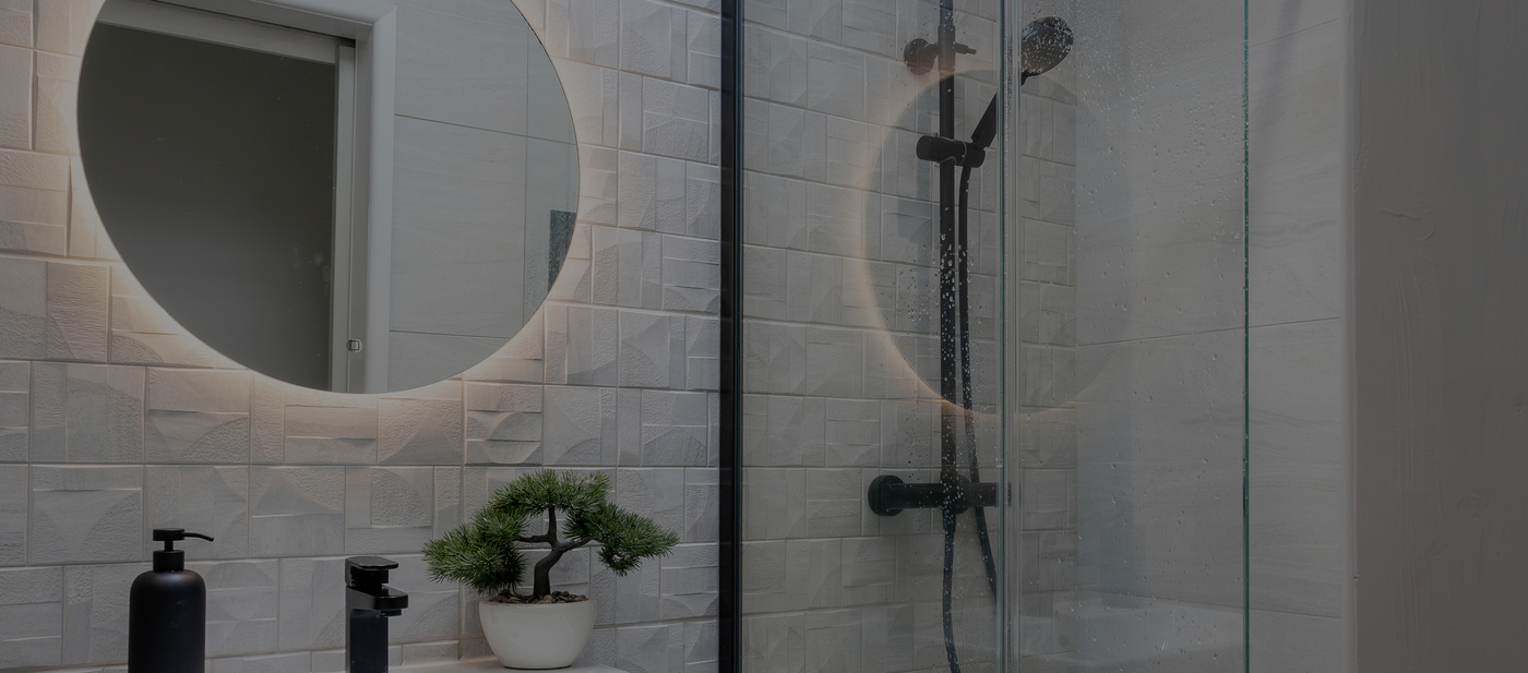 Modern bathroom with circular backlit mirror, black fixtures, and a small potted plant on the countertop.