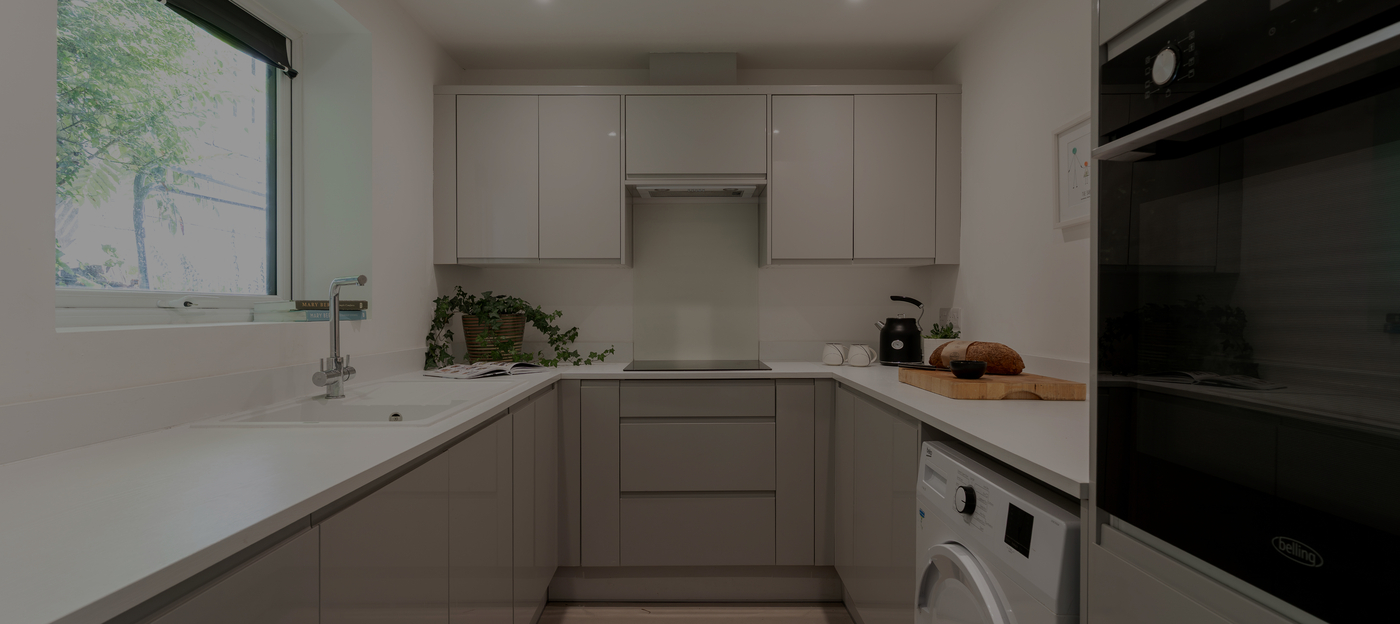 Modern white kitchen with sleek cabinets, countertop plants, and appliances, offering a bright and minimalist design.