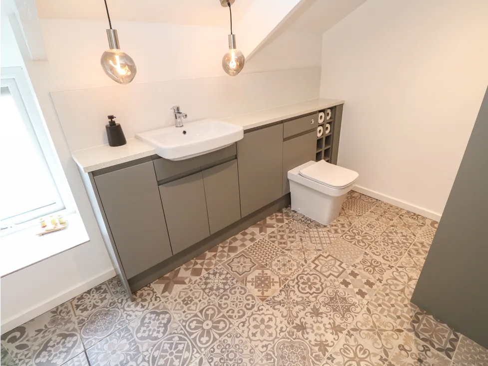 Modern bathroom with patterned tiles, grey cabinets, and pendant lighting.