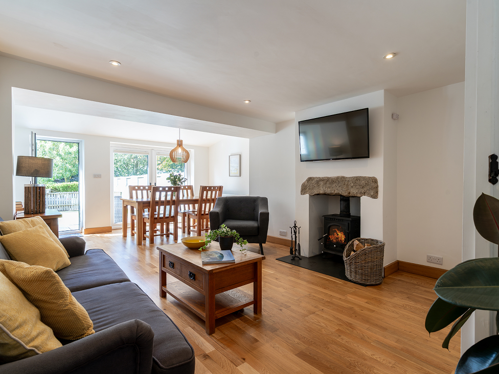 Bright open-plan living and dining room with cozy fireplace, wooden floor, and modern furniture overlooking a garden.