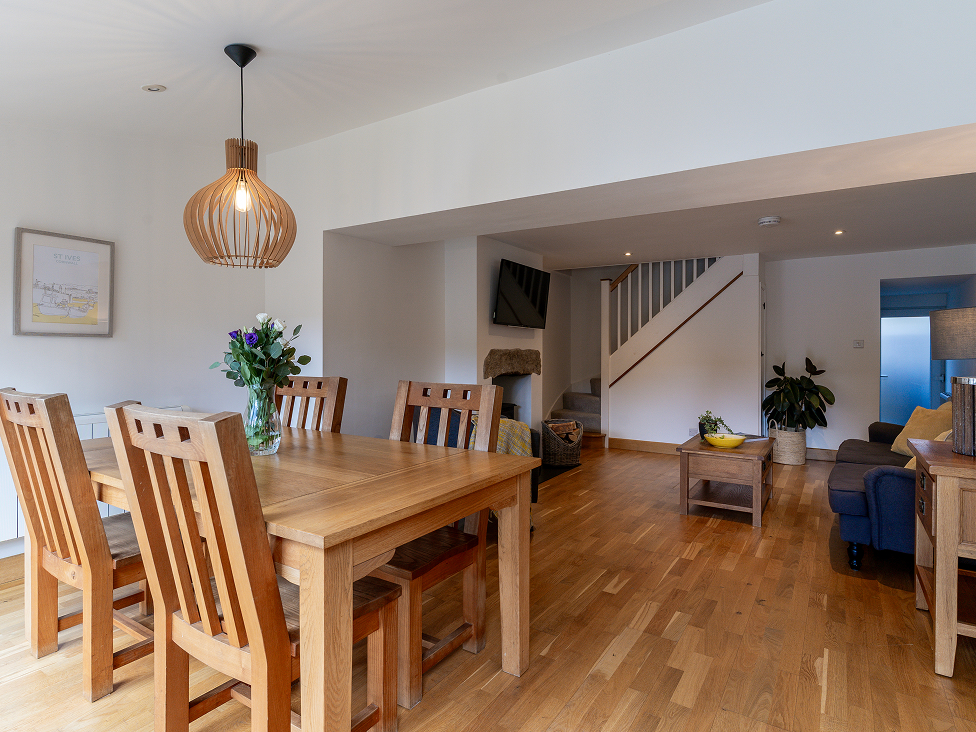 Modern open-plan dining and living area with wooden floors, table, and chairs, featuring stylish lighting and decor.