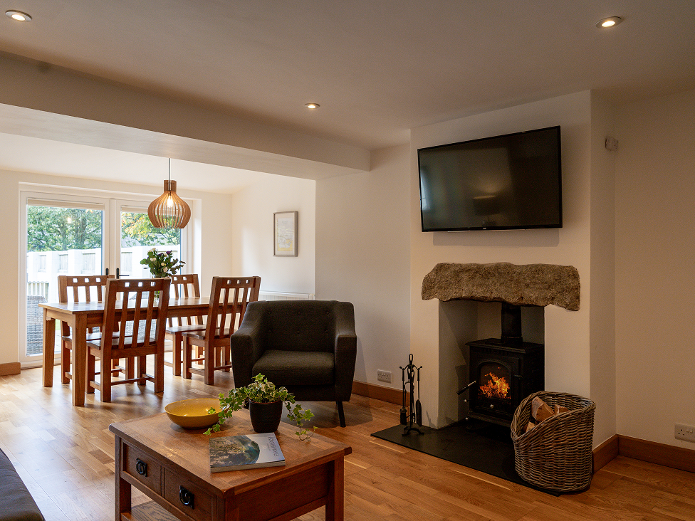 Cozy living-dining room with wood stove, TV, and modern decor. Elegant wooden furniture and glass doors enhance the space.