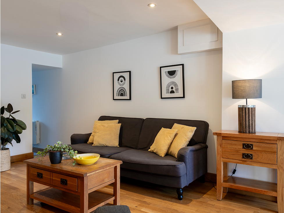 Modern living room with grey sofa, yellow pillows, wooden furniture, abstract art, and cozy lighting.