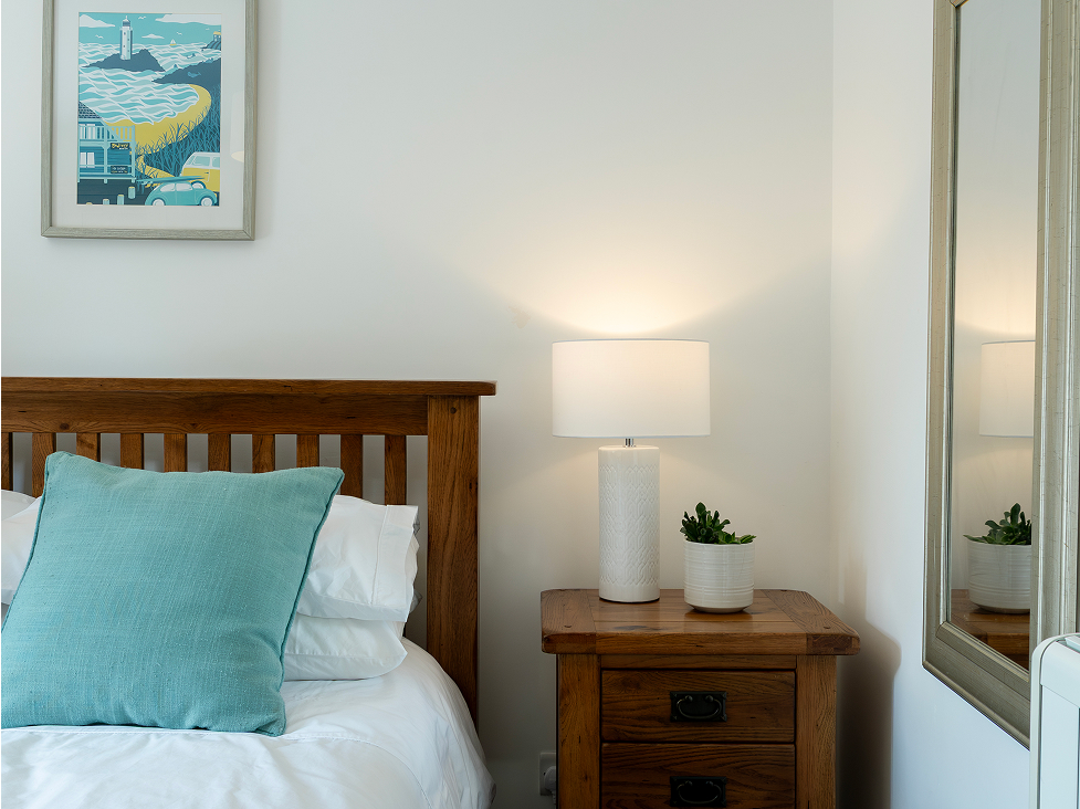 Cozy bedroom with wooden bed, blue pillow, bedside lamp, and potted plant for a serene ambiance.