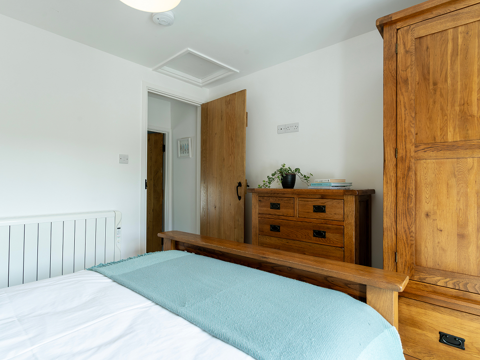 Cozy bedroom with wooden furniture, green bedspread, and white walls, creating a tranquil, modern atmosphere.