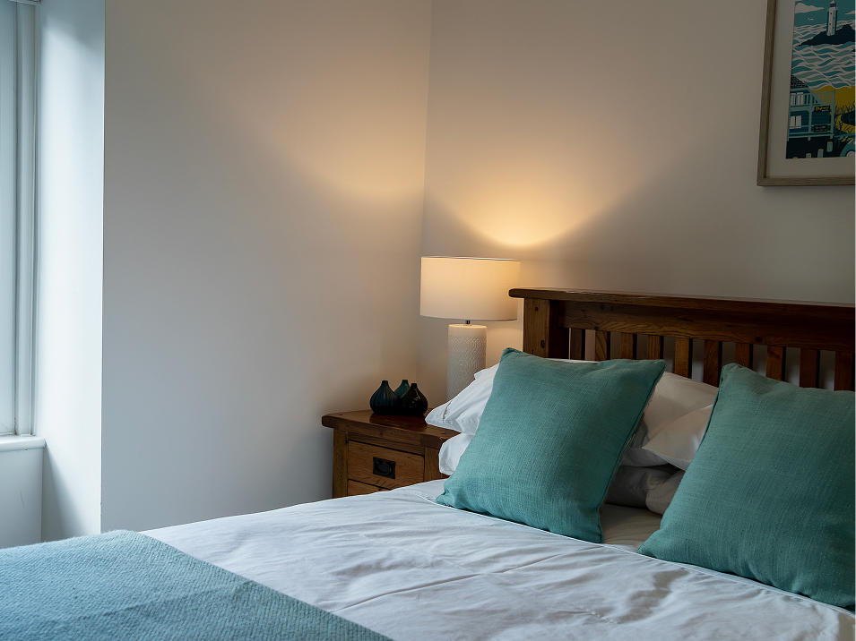 Cozy bedroom with soft lighting, wooden bed frame, and teal pillows perfect for relaxation and comfort.