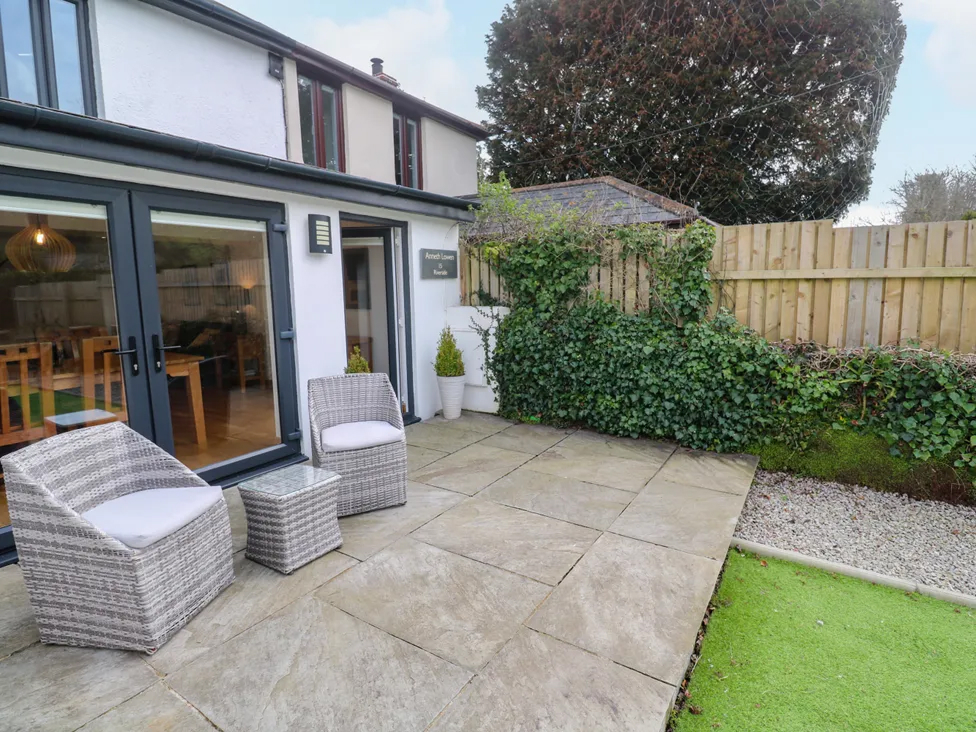 Modern patio with wicker chairs and glass table, featuring a fenced garden and outdoor dining area.