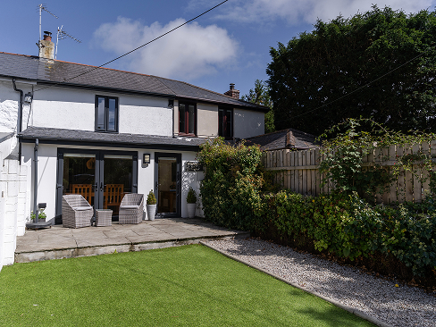 Cozy backyard with patio seating, lush greenery, and a modern house under a clear blue sky.