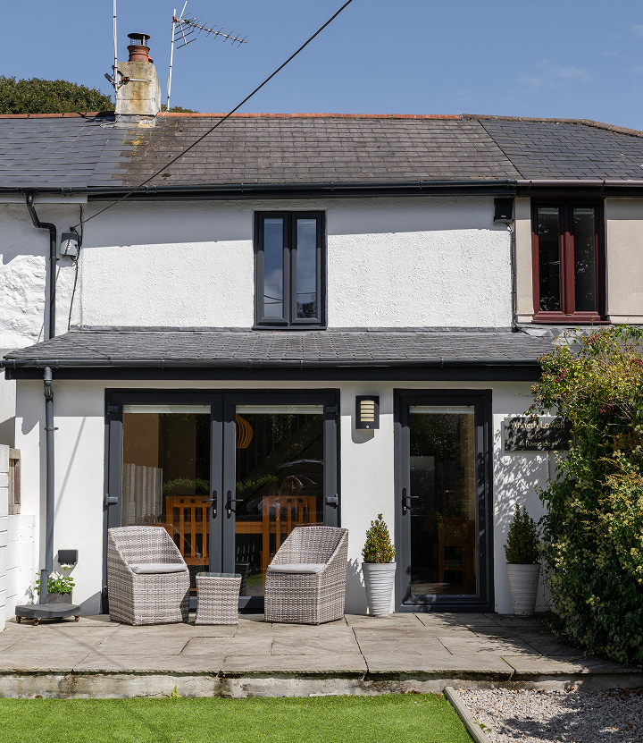 Cozy cottage patio with wicker chairs and French doors, ideal for relaxing in a serene green garden setting.