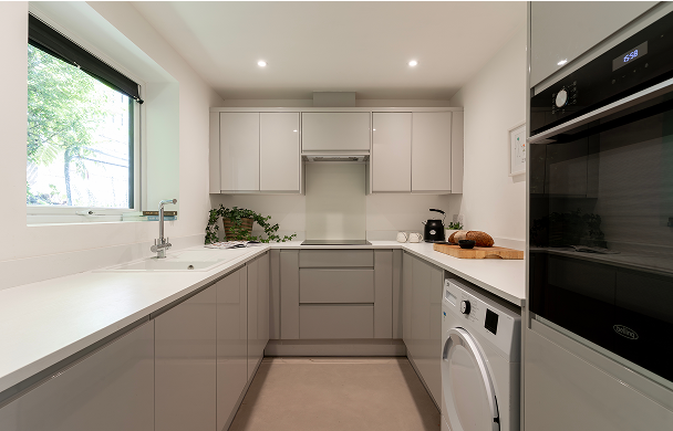 Modern kitchen with sleek grey cabinets, large window, and appliances, offering a clean and bright cooking space.