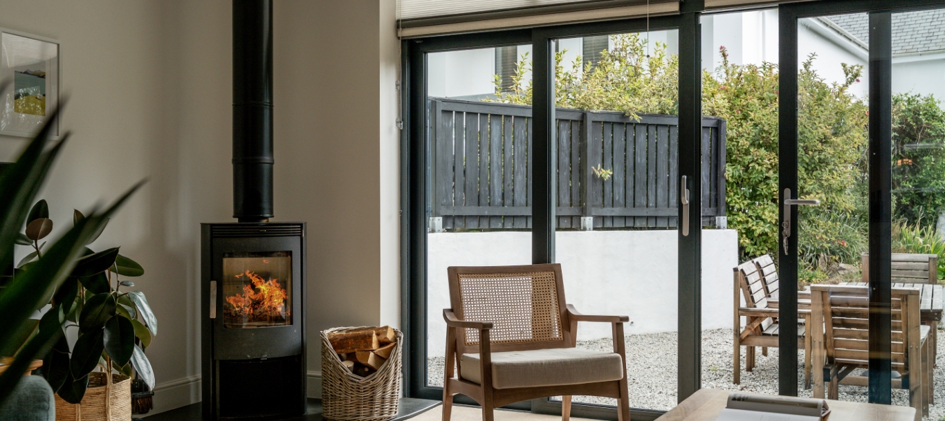 Cozy living room with a wood-burning stove, large glass doors, and a wooden chair overlooking a garden patio.