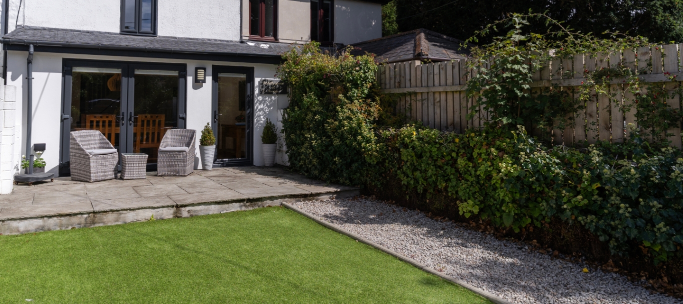 Cozy patio with wicker chairs, lush garden, and neat lawn outside a charming house.