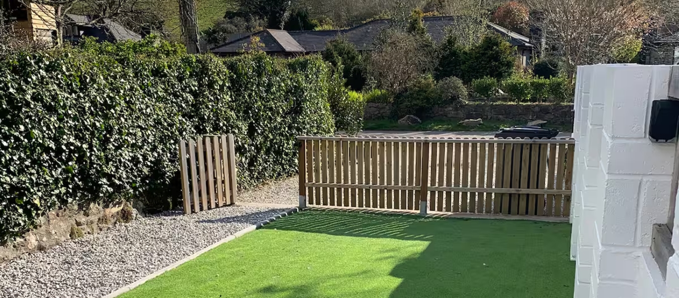 Backyard with green lawn, wooden fence, and gravel path under sunny sky.