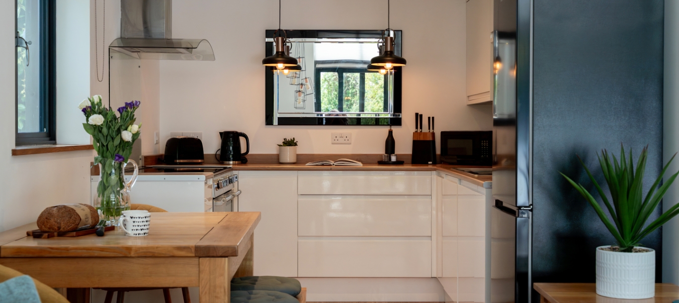 Modern kitchen with wooden table, flowers, bread loaf, pendant lights, and sleek appliances. Cozy and stylish design.