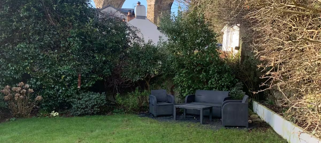 Outdoor patio with black furniture set against lush greenery and stone arches in the background.