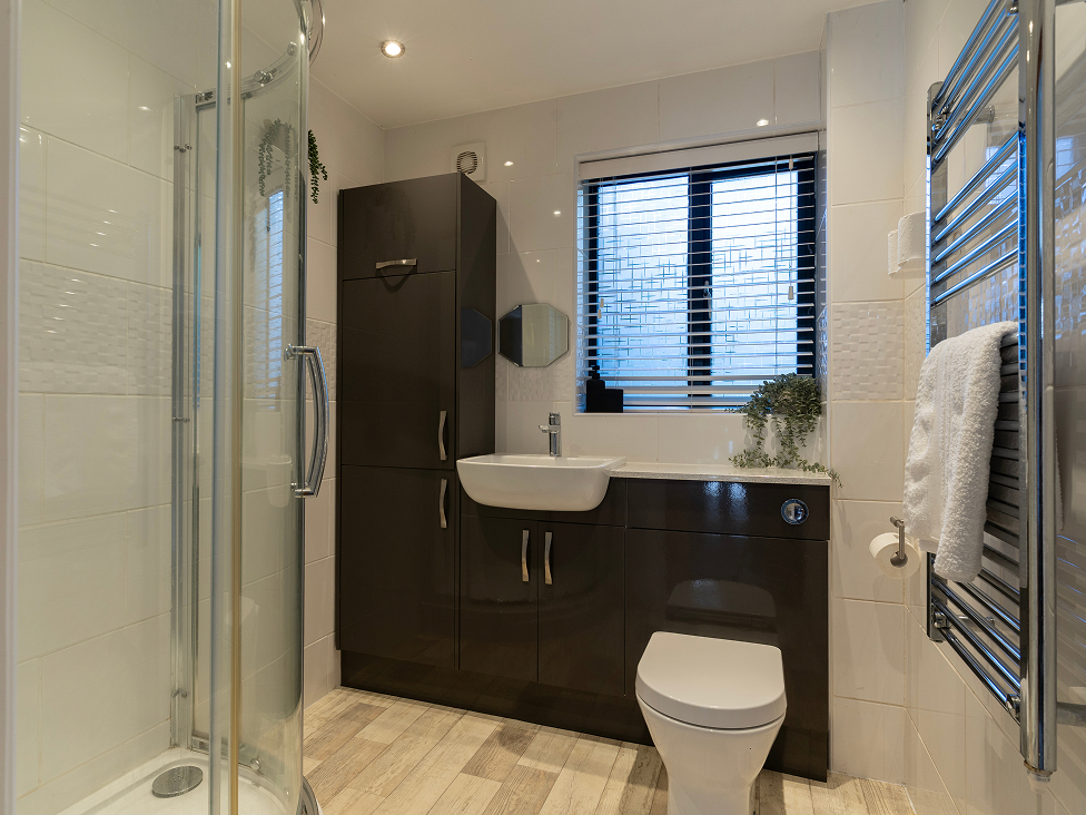 Modern bathroom with shower, sink, toilet, and towel rack, featuring sleek design and wood flooring.