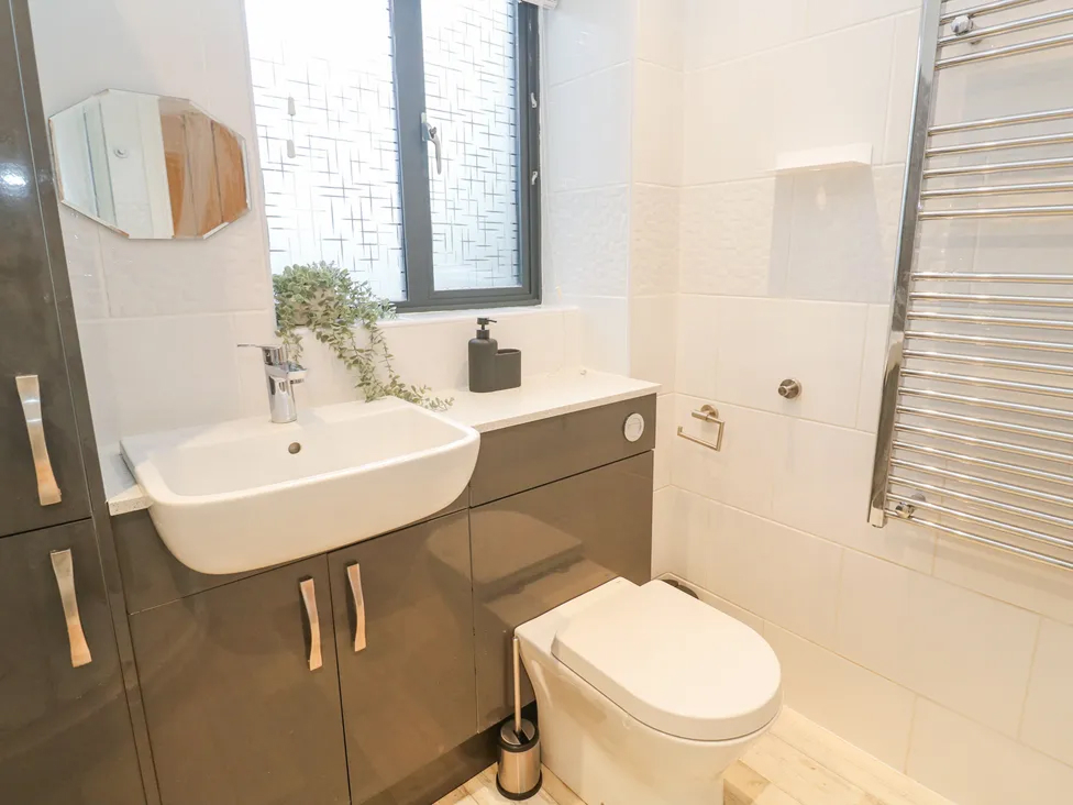 Modern bathroom with a sleek sink, toilet, and plants. Bright window and towel rack enhance the clean design.