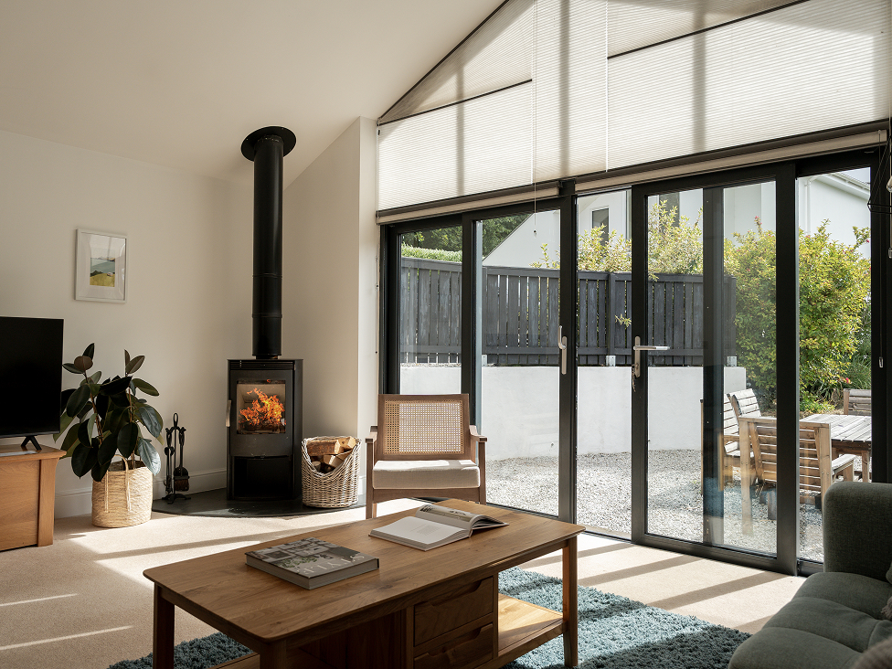 Modern living room with fireplace, large windows, and cozy decor. Bright natural light fills the minimalist space.