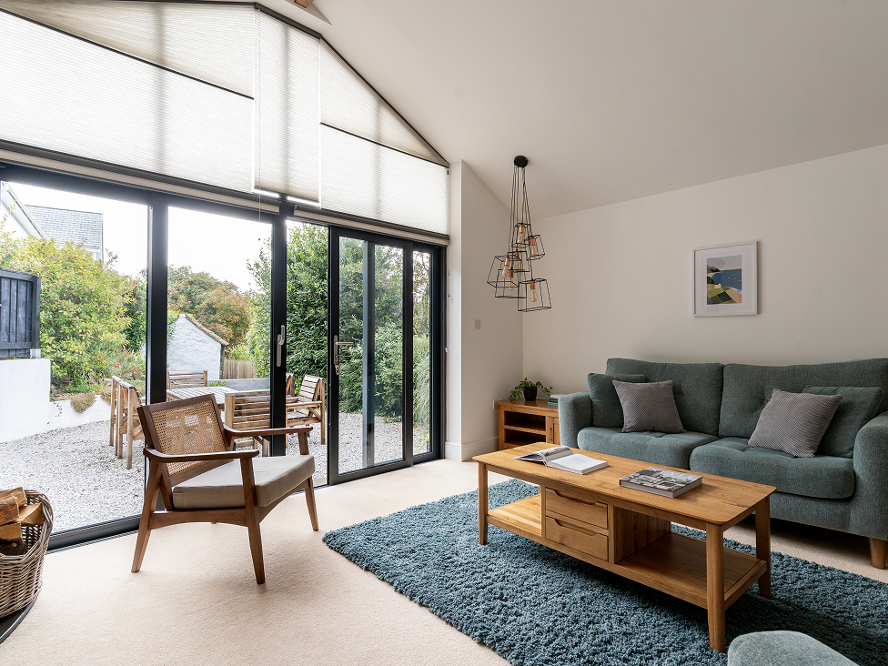 Modern living room with large windows, blue sofa, wooden furniture, and outdoor garden view.