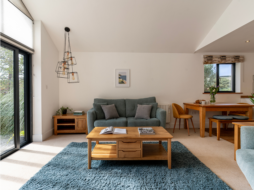 Modern living room with blue sofa, wooden furniture, large window, and stylish lighting. Cozy and inviting space.