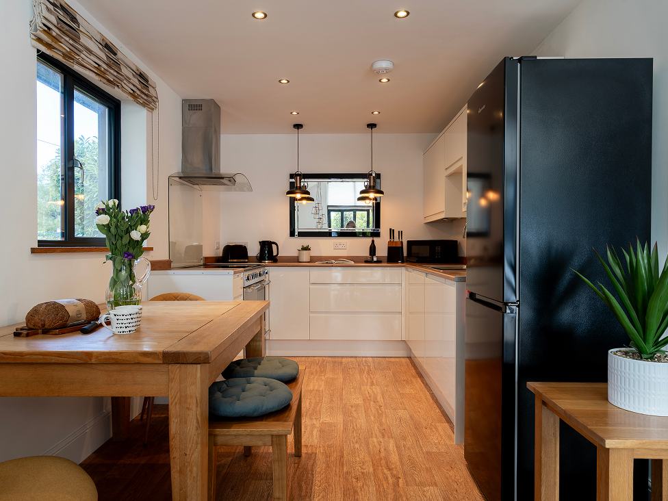 Modern kitchen with wooden flooring, table, and stools. White cabinets, black fridge, and potted plants enhance the decor.