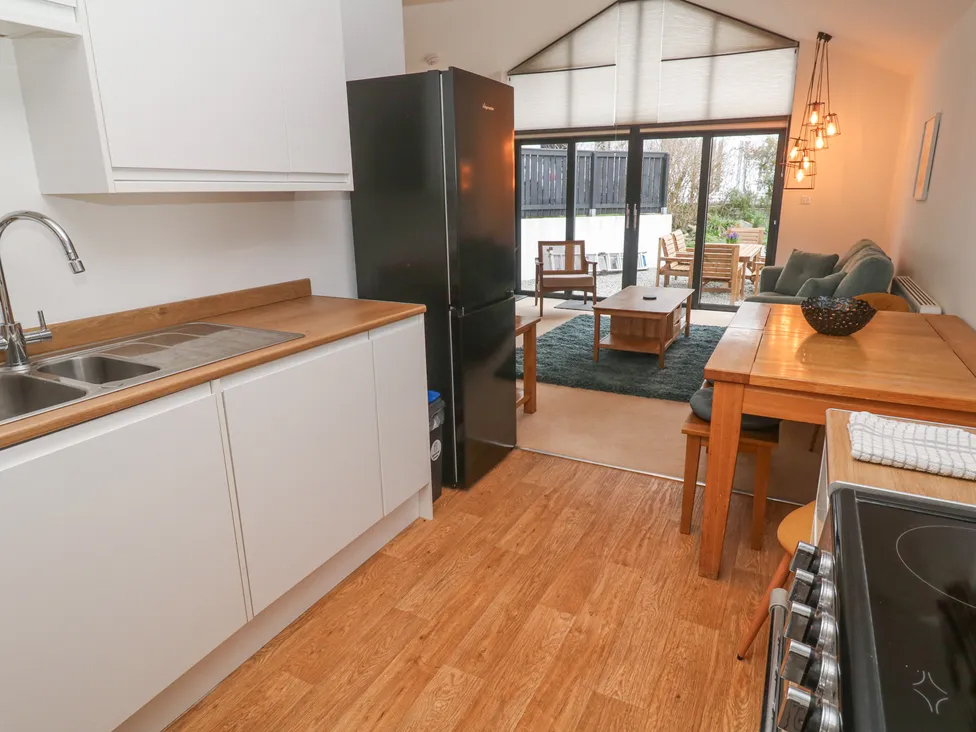Modern open-plan kitchen and living room with wooden floors, black fridge, and cozy seating area by large windows.