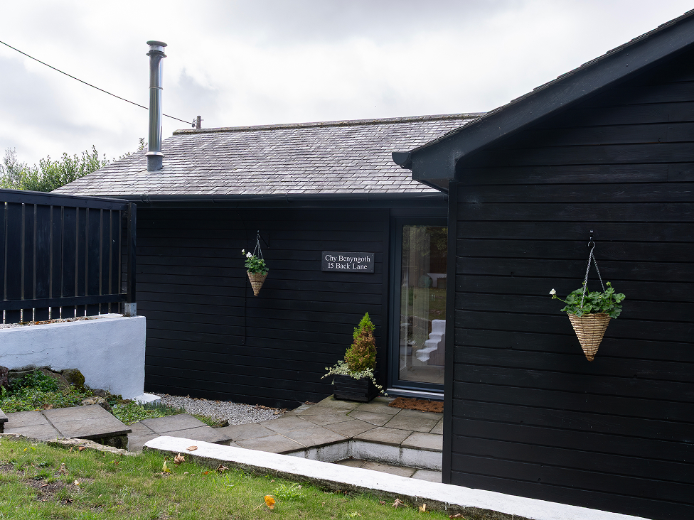 Black wooden house exterior with hanging plants and slate roof, showcasing modern rustic design.