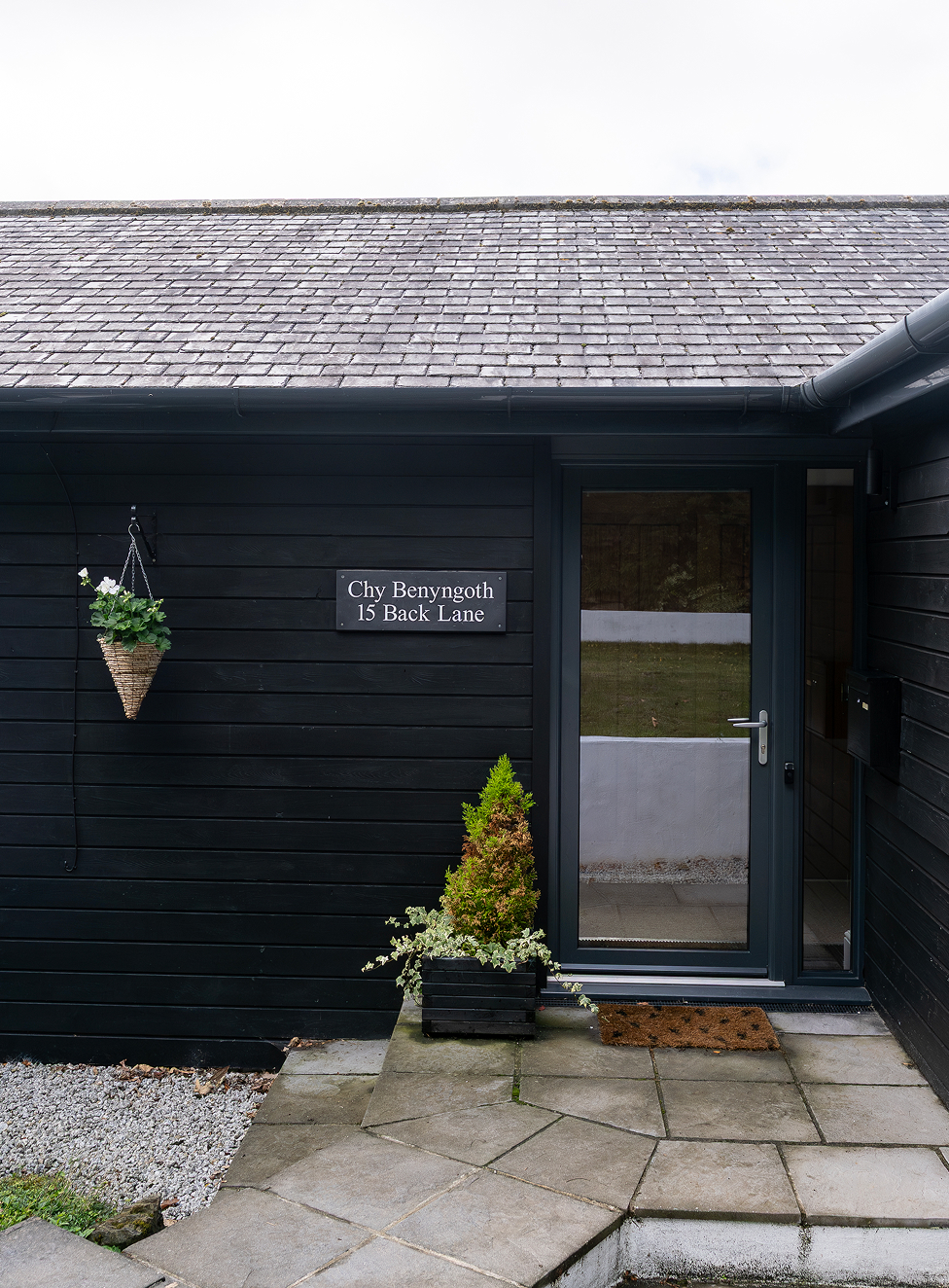 Modern black house entrance with potted plants and a hanging basket at 15 Back Lane.