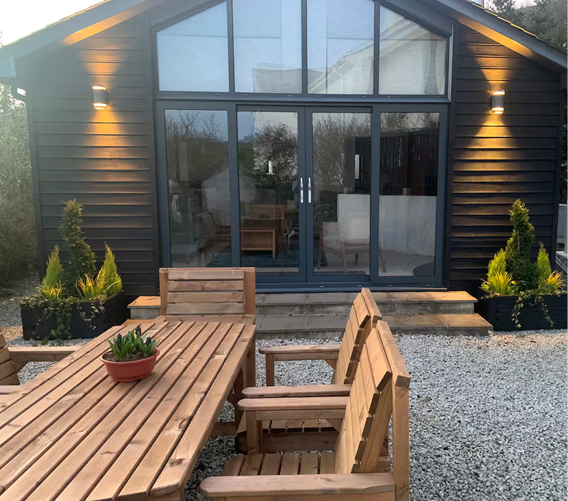 Modern garden room with glass doors and wooden patio furniture. Cozy outdoor space with greenery accents.